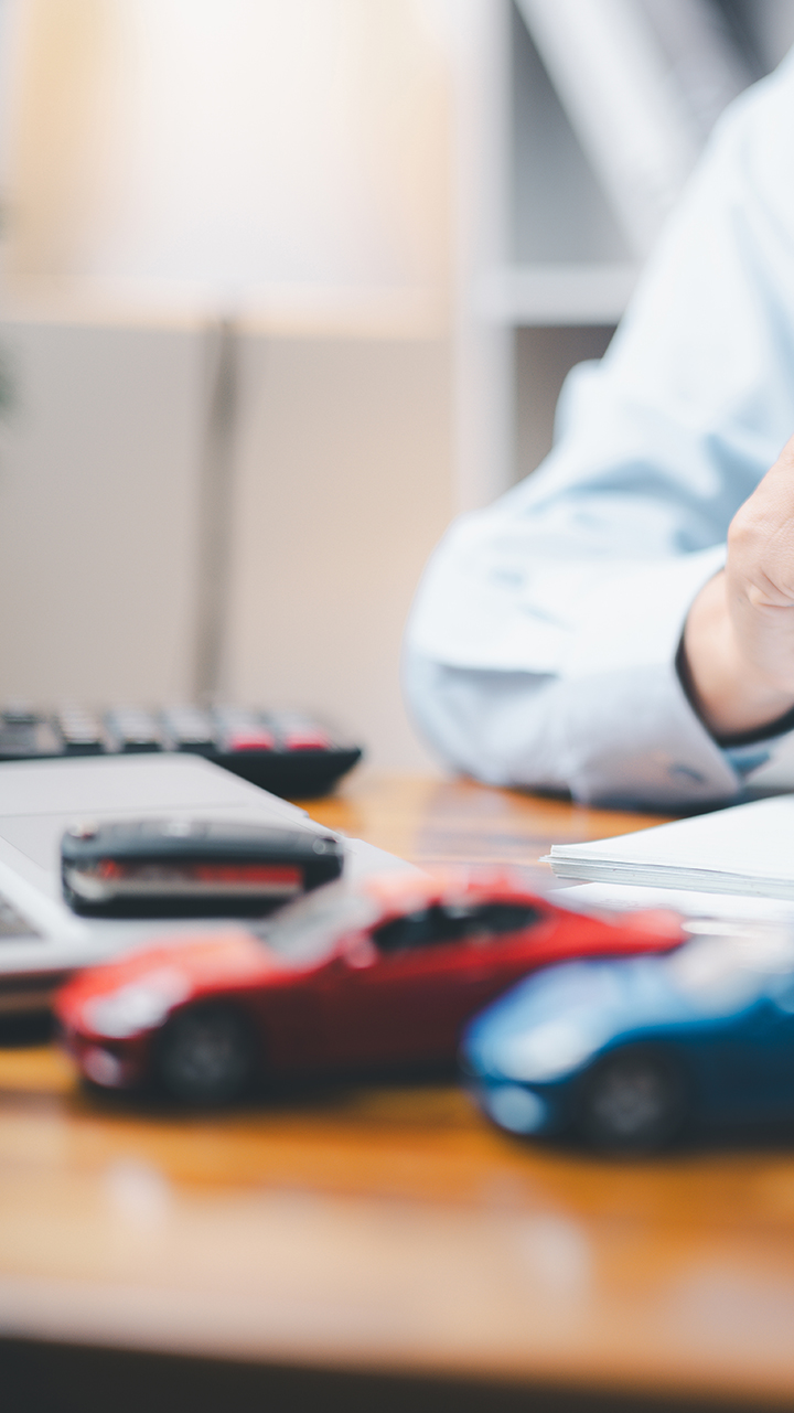 Man at table with tablet and miniature car models, symbolizing choice of insurance solutions
