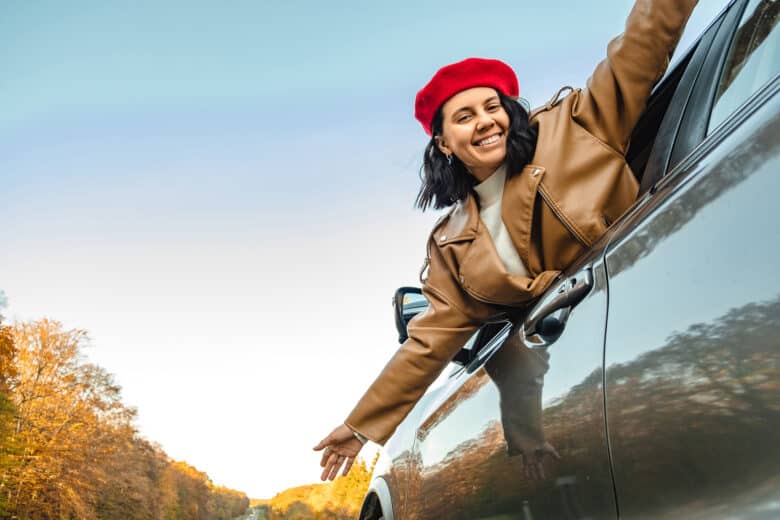 Happy woman in red beret leaning out of car window, enjoying the ride