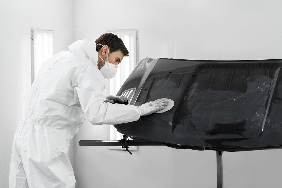 Speciālists slīpē auto detaļu pirms krāsošanas